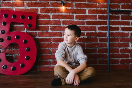 Boy sitting in the studio on a background of a brick wallの写真素材