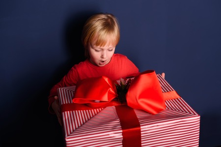 The child is in the hands holds a big gift box on a striped backgroundの写真素材