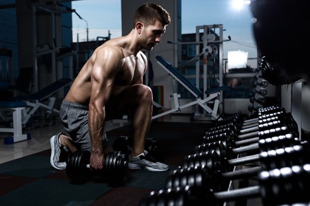 Young bodybuilder working out with bumbbells weights at the gymの写真素材