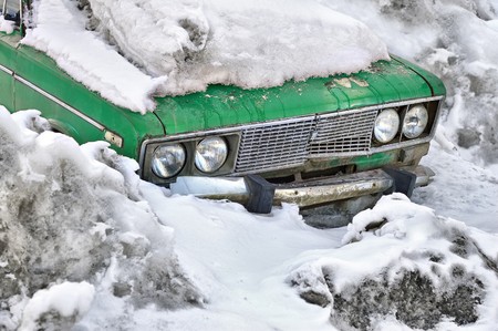 Old green car under snow in winterの写真素材