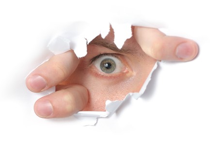 Eye looking through a hole in a paperの写真素材