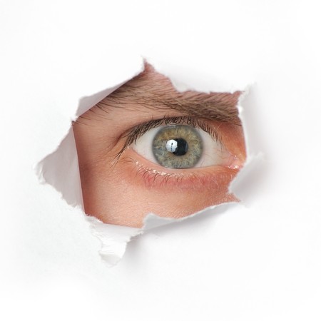 Eye looking through a hole in a paperの写真素材