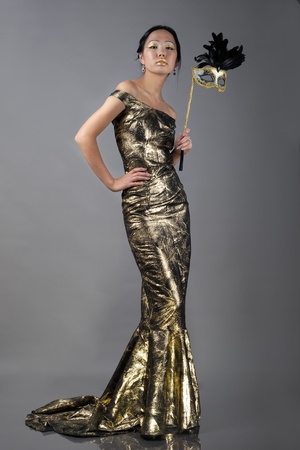 Asian woman with carnaval mask in golden evening dressの写真素材
