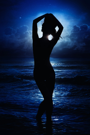Silhouette of young lady on a beach at nightの写真素材