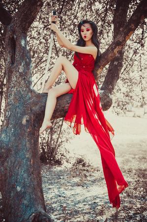 Asian woman in beautiful red dress sitting on treeの写真素材
