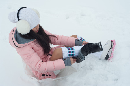 Girl puts on skates outdoors at winter