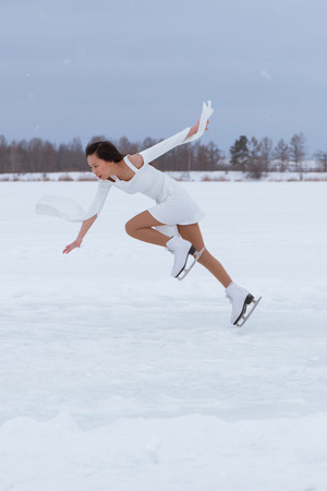 Pretty young woman on skates in white dress at winter frozen park outdoorsの写真素材