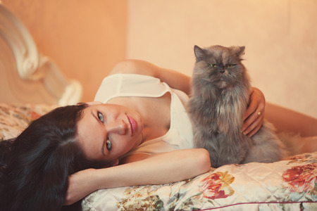 Pretty young woman with her cat lying on the bedの写真素材