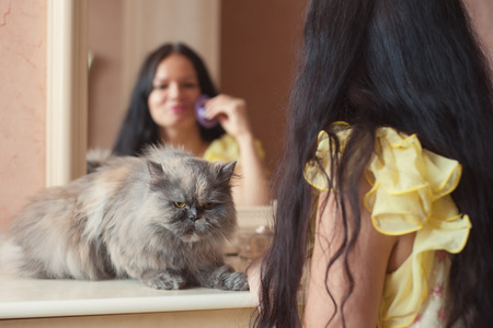 Portrait of woman with cat in yellow dress indoors near mirrorの写真素材