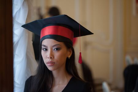 Portrait of young asian woman in graduation cap indoors