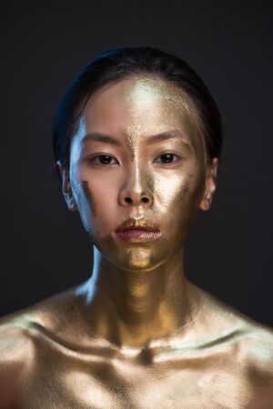 Portrait of young asian woman in golden paint at studio with black background