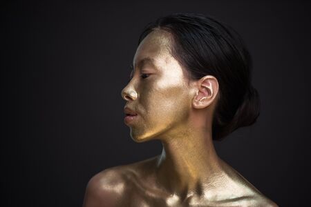 Portrait of young asian woman in golden paint at studio with black background