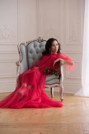 Beautiful asian pregnant woman in long red dress indoorsの写真素材