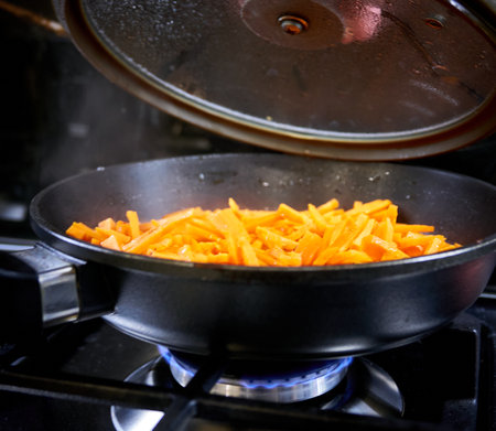 Fried carrots in a frying pan on a gas stove in the kitchenの写真素材
