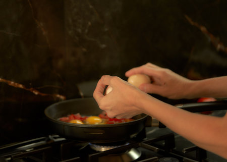 Closeup of female hands cooking eggs in frying pan on gas stoveの写真素材