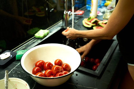 Woman washing tomatoes in a sink in a kitchen. Selective focus.の写真素材