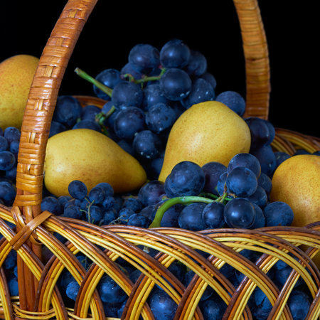 Wicker basket with fresh ripe pears and grapes isolated on black backgroundの写真素材