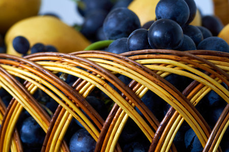 Wicker basket full of fresh ripe grapes and plums closeupの写真素材