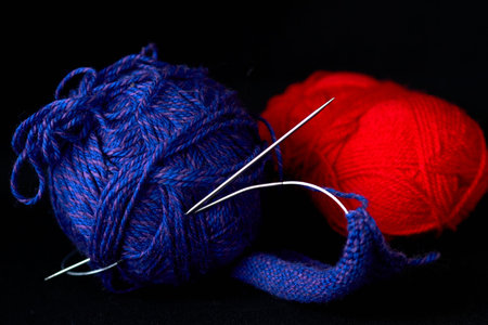 Two skeins of yarn and knitting needles on a black background.