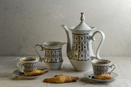 Coffee pot and cups with coffee on the table with a light linen tablecloth with cookies on a light backgroundの写真素材
