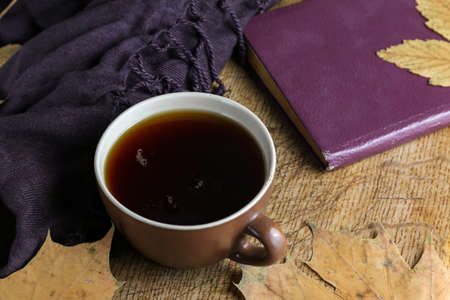 A cup of black tea on a table with a book and a shawlの写真素材