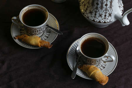Coffee pot and cups with coffee on a table with a dark linen tablecloth with cookies on a dark backgroundの写真素材