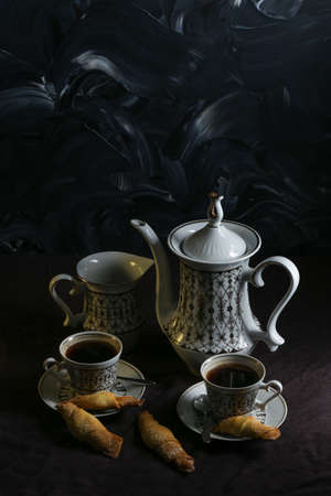 Coffee pot and cups with coffee on a table with a dark linen tablecloth with cookies on a dark backgroundの写真素材