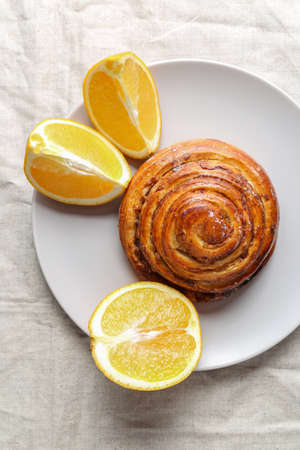 Cinnamon rolls on a gray plate on a bright table with a bowl of walnuts and orangeの写真素材
