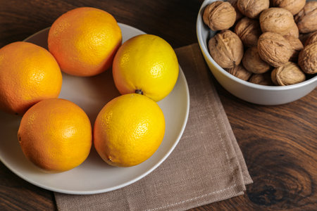Lemons, oranges and walnuts in a gray bowl on a wooden tableの写真素材