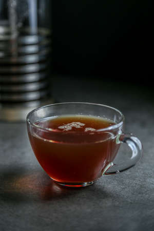 A cup of hot black tea in a glass cup and a kettle press on a gray ceramic countertop.の写真素材