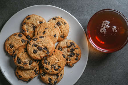 A cup of hot black tea in a glass cup and a gray ceramic plate with cookies with chocolate chips on a gray ceramic tabletopの写真素材