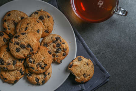 A cup of hot black tea in a glass cup and a gray ceramic plate with cookies with chocolate chips on a gray ceramic counter top with a gray linen napkin.の写真素材