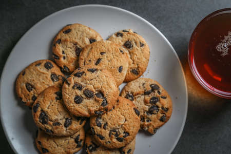 A cup of hot black tea in a glass cup and a gray ceramic plate with cookies with chocolate chips on a gray ceramic tabletopの写真素材
