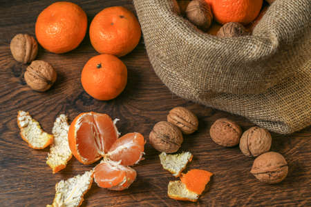 Ripe, tasty and juicy oranges, tangerines in a canvas bag with walnuts on the table.の写真素材