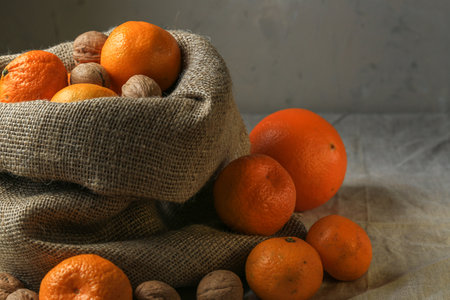 Ripe, tasty and juicy oranges, tangerines in a canvas bag with walnuts on the table.の写真素材