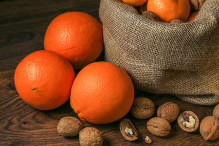 Ripe, tasty and juicy oranges, tangerines in a canvas bag with walnuts on the table.の写真素材