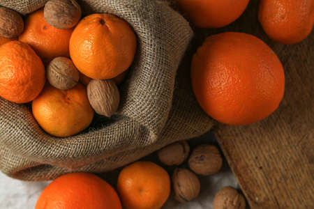 Ripe, tasty and juicy oranges, tangerines in a canvas bag with walnuts on the table.の写真素材