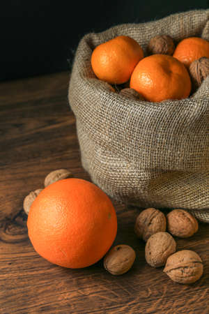Ripe, tasty and juicy oranges, tangerines in a canvas bag with walnuts on the table.の写真素材