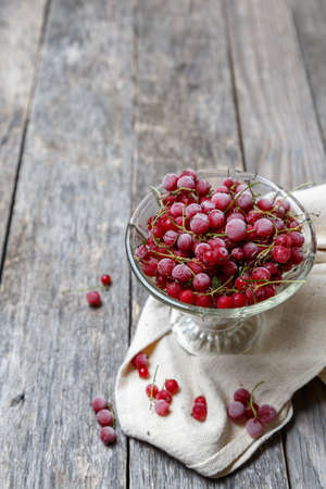 Frozen red currants in a glass vase on a cloth on a rustic wooden table. Close-up. Natural and...