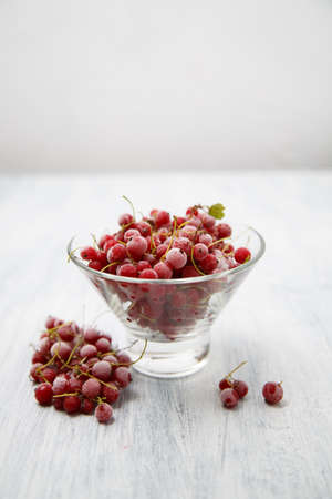 Frozen red currants in a glass vase on a white wooden table. Close-up. Natural and healthy frozen berry rich in vitamins.の写真素材