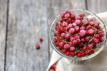 Frozen red currants in a glass vase on a cloth on a rustic wooden table. Close-up. Natural and...