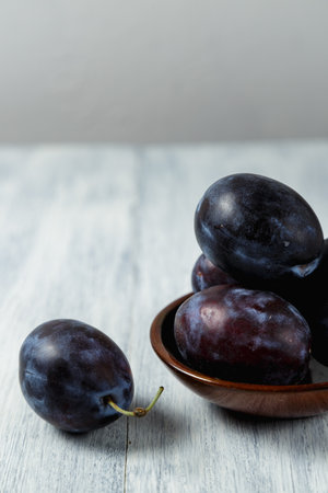 Blue plum in a plate on a wooden table. Place for text. Fruit background with copy space. Still life food.の写真素材
