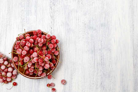 Frozen red currants in a brown ceramic vase on a white wooden table. Close-up. Natural and healthy frozen berry rich in vitamins.の写真素材