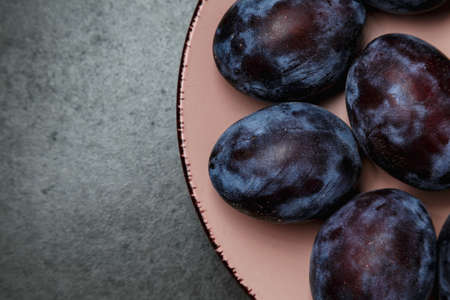 Blue plum in a plate on a dark background. Top view, place for text. Fruit background with copy space. Still life food.の写真素材