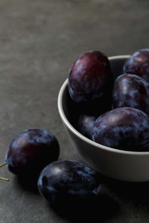 Blue plum in a bowl on a dark background. Place for text. Fruit background with copy space. Still life food.の写真素材