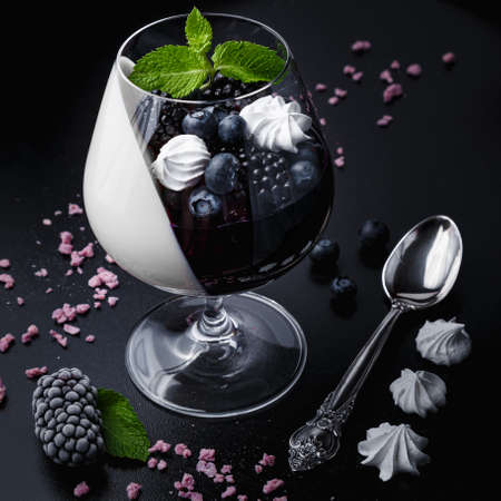 Blackberry panna cotta in glasses on a black background. Traditional Italian dessert with blackberry jelly and mint leaf.の写真素材