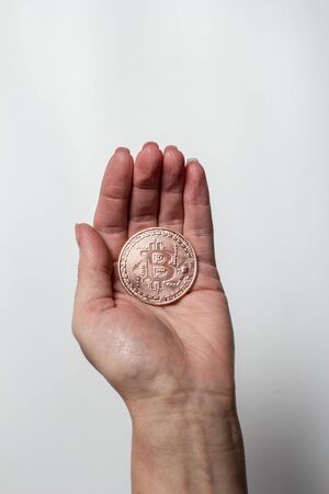 Bronze bitcoin is held by a hand on a white backgroundの写真素材