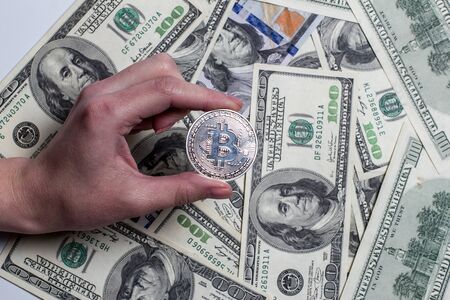Man holds silver bitcoin on a background of money.