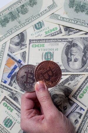 Two bitcoins in hand on a background of dollars