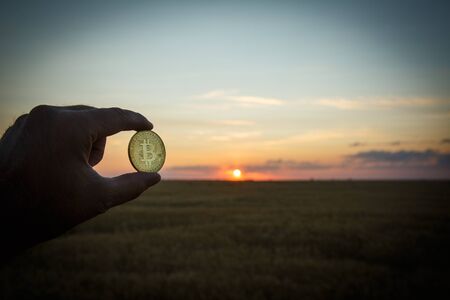 Bitcoin in the hand of a man at sunsetの写真素材